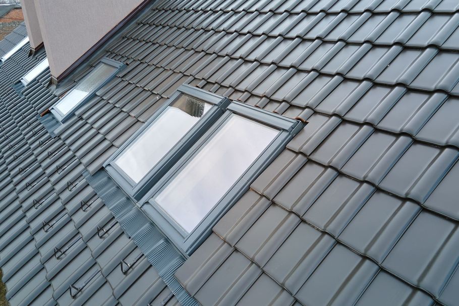 A view of a grey tiled roof featuring several skylights set into the slope near a chimney.