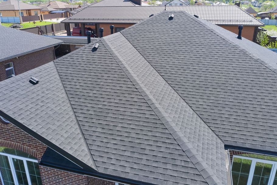 A high-angle view of a grey shingled roof on a brick house, featuring multiple gables and several roof vents.