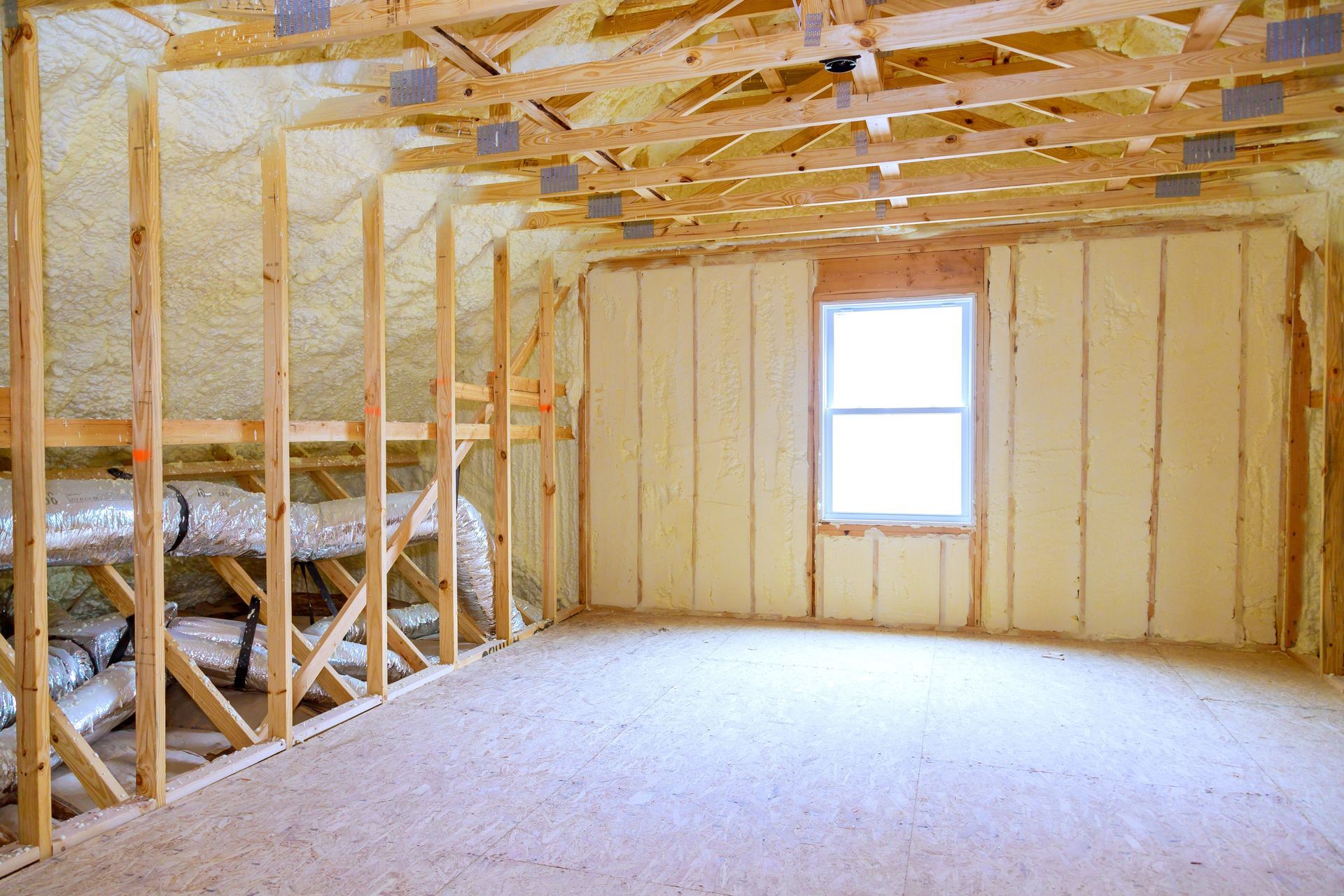 Unfinished attic space with insulation, wooden wall studs, exposed ceiling rafters, and a centered window.