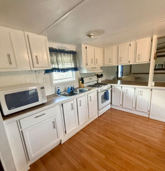 Kitchen with white cabinets, appliances, and wooden floor. A microwave, stove, and sink are visible.