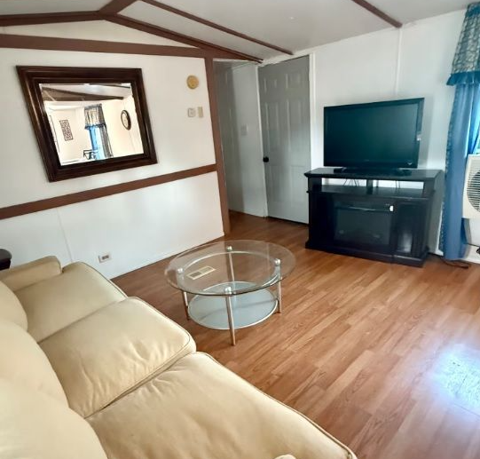 Living room with tan couch, glass table, TV on stand, mirror, and door.