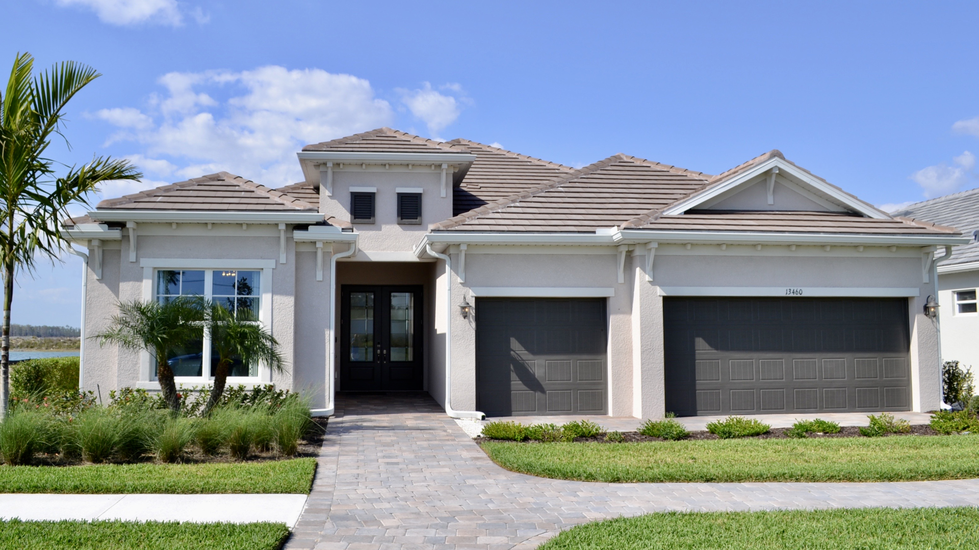 A large white house with two garages and a palm tree in front of it.