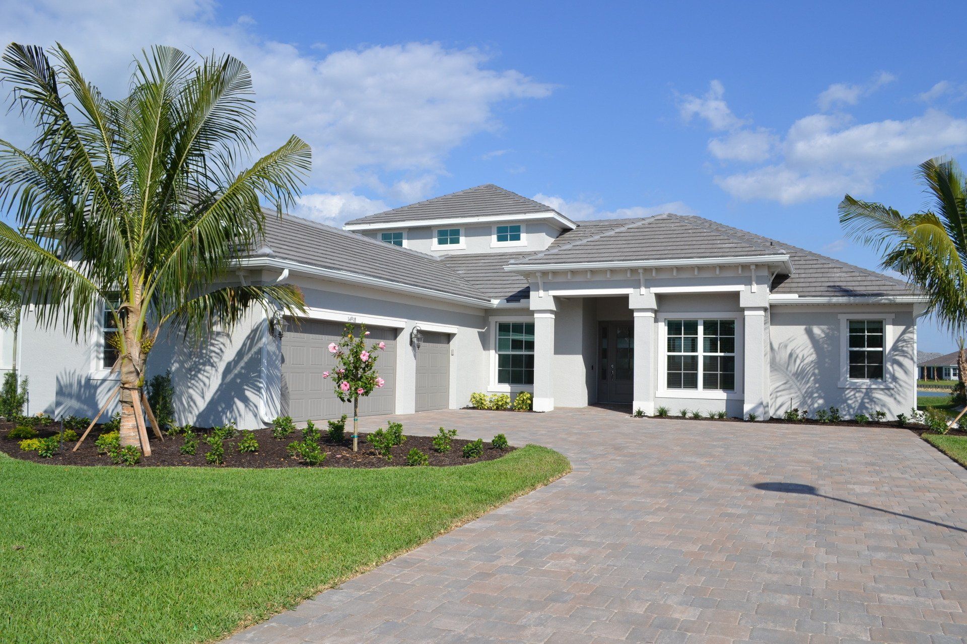 A large white house with a brick driveway and palm trees in front of it