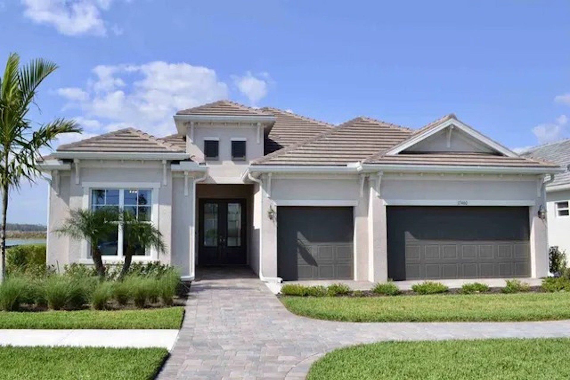 A large white house with two garages and a brick driveway.