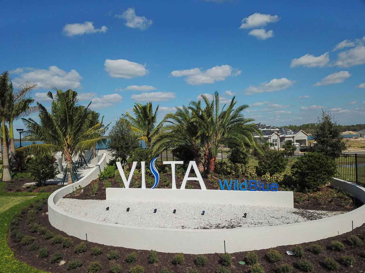 A vista sign is surrounded by palm trees and bushes.