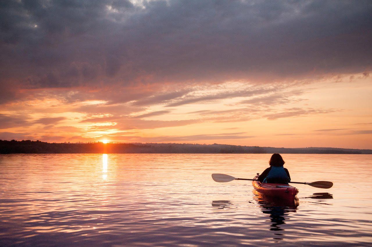 A person is paddling a kayak on a lake at sunset.