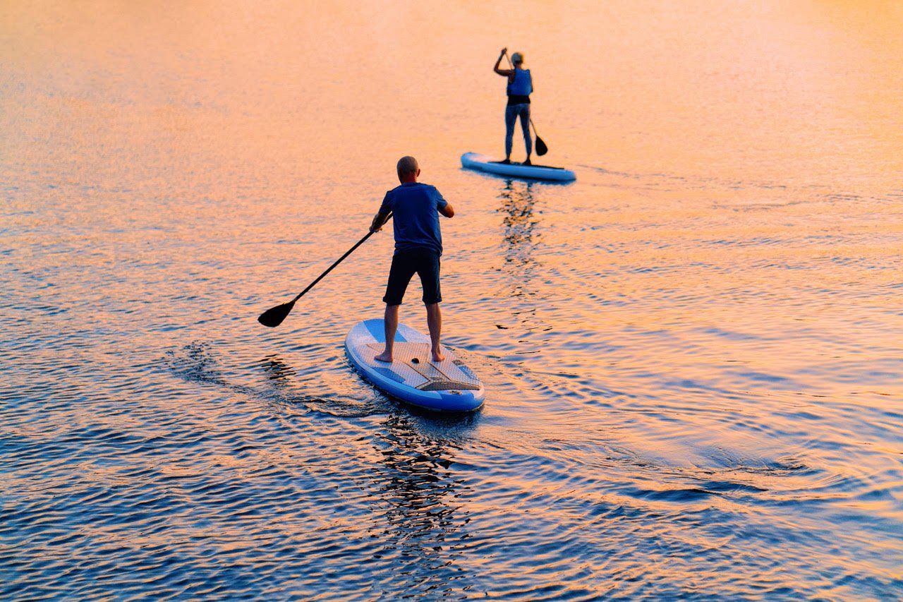 Two people are riding paddle boards in the water at sunset.