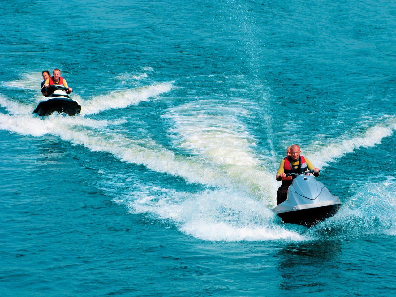 Two people are riding jet skis in the ocean.