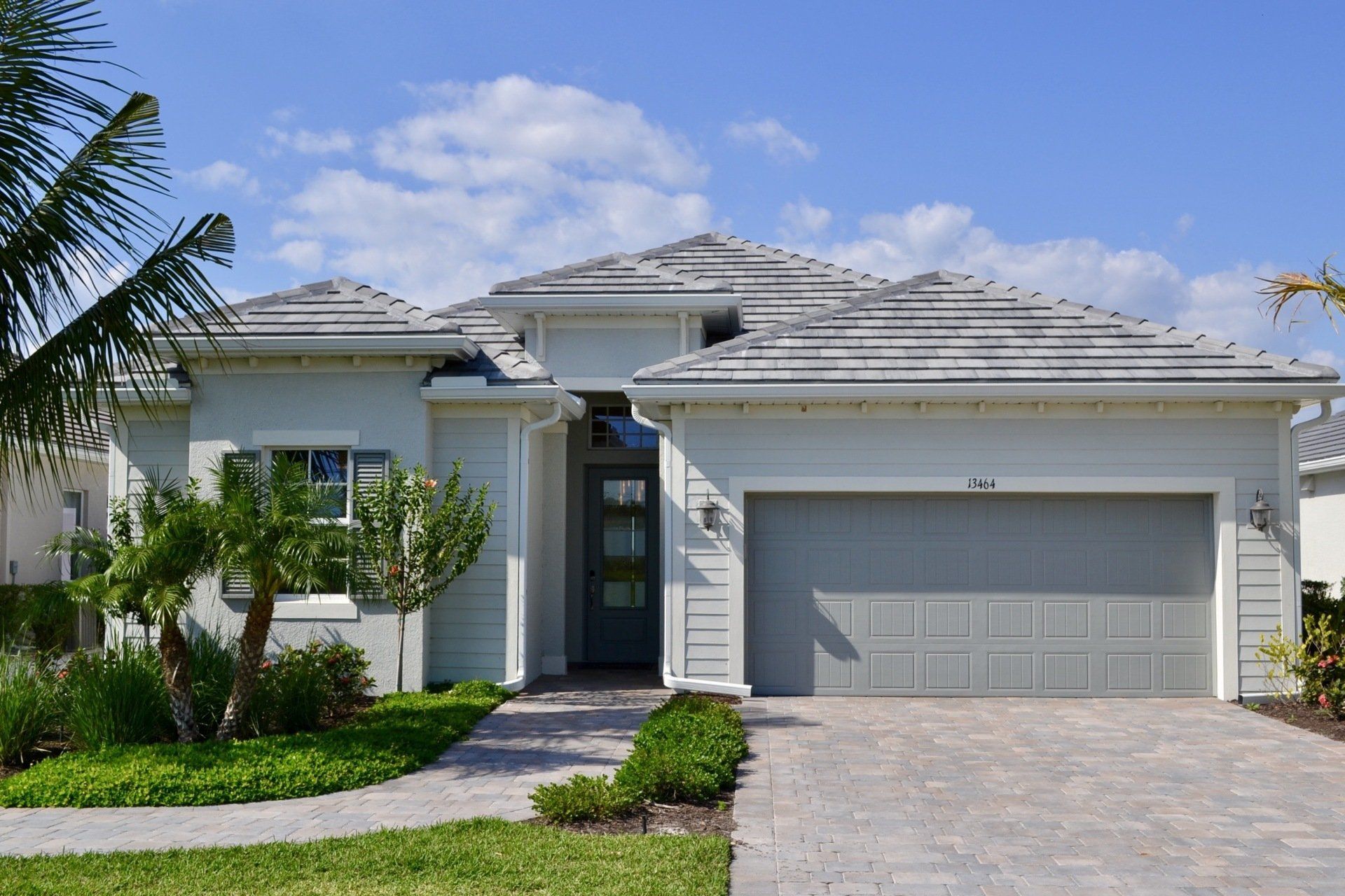 A white house with a gray garage door and a palm tree in front of it.