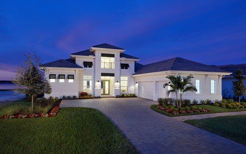 A large white house is sitting on top of a lush green lawn next to a body of water.