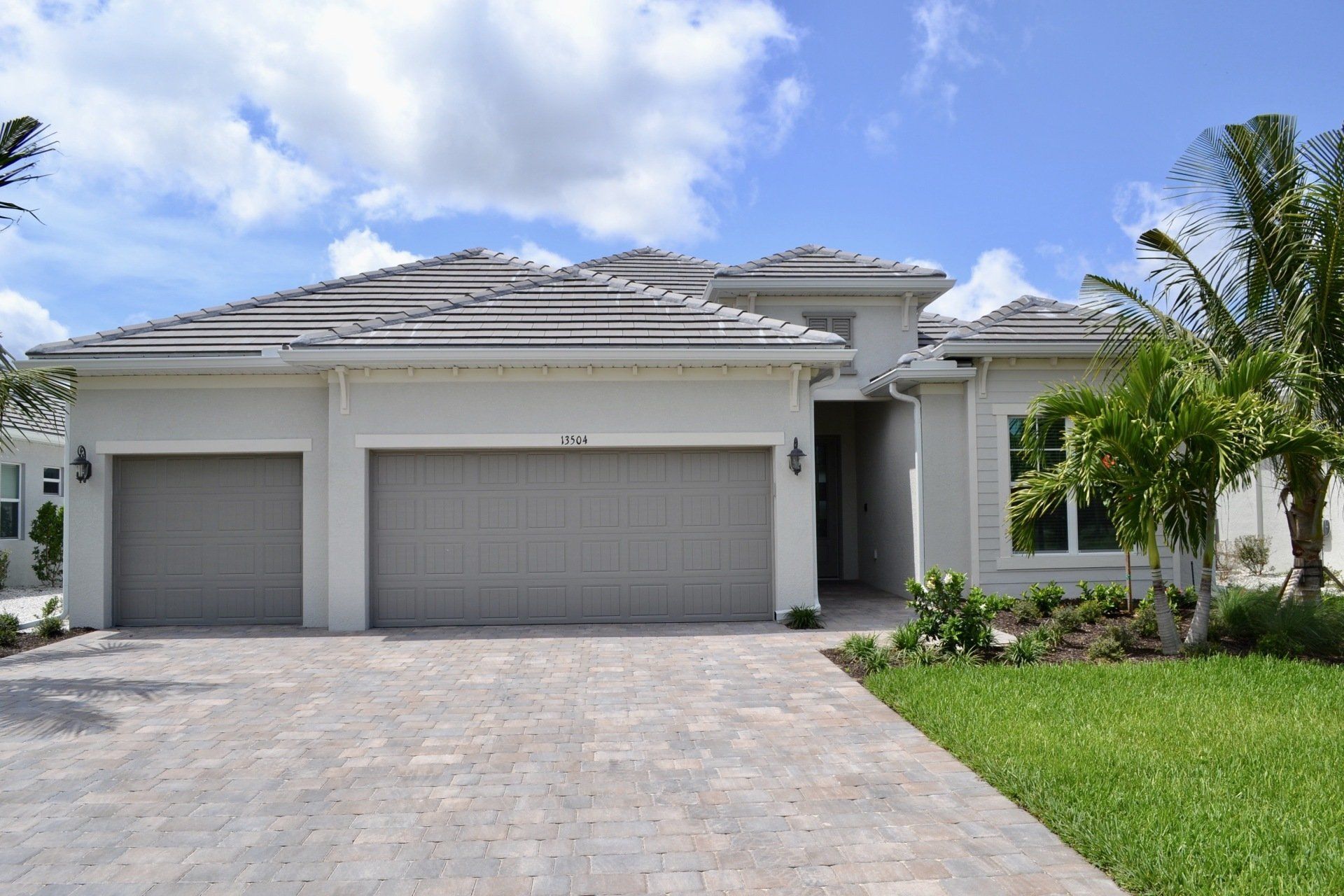 A white house with three garage doors and a brick driveway