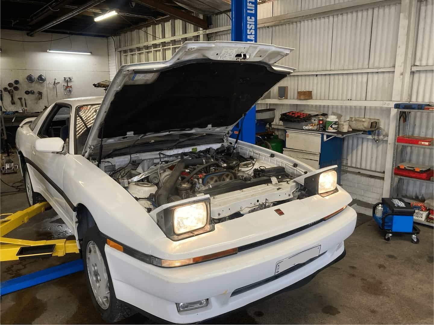 A White Car With The Hood Up Is On A Lift In A Garage — NEID Automotive In North Gosford, NSW