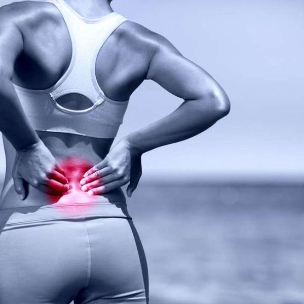 Woman in athletic wear holding her lower back, indicating pain. Red highlighting pain area.