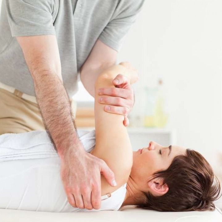 A woman lies on a table while a person performs arm therapy, indoors.