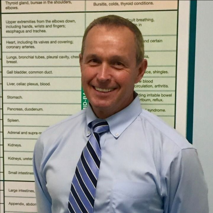 Man smiling in front of a chart with medical terms. He is wearing a light blue shirt and striped tie.