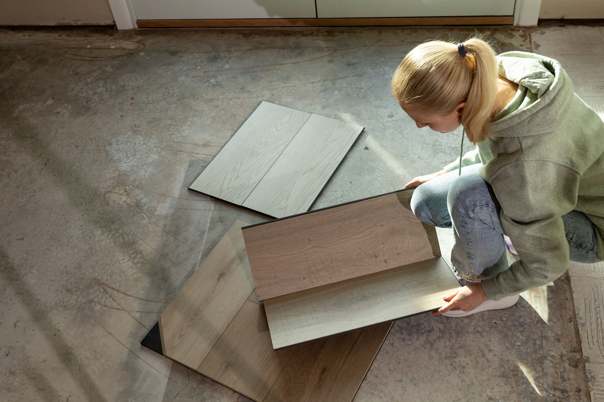 Woman holding luxury vinyl wood samples on a concrete floor, selecting waterproof flooring options Woman holding luxury vinyl wood samples on a concrete floor, selecting waterproof flooring options