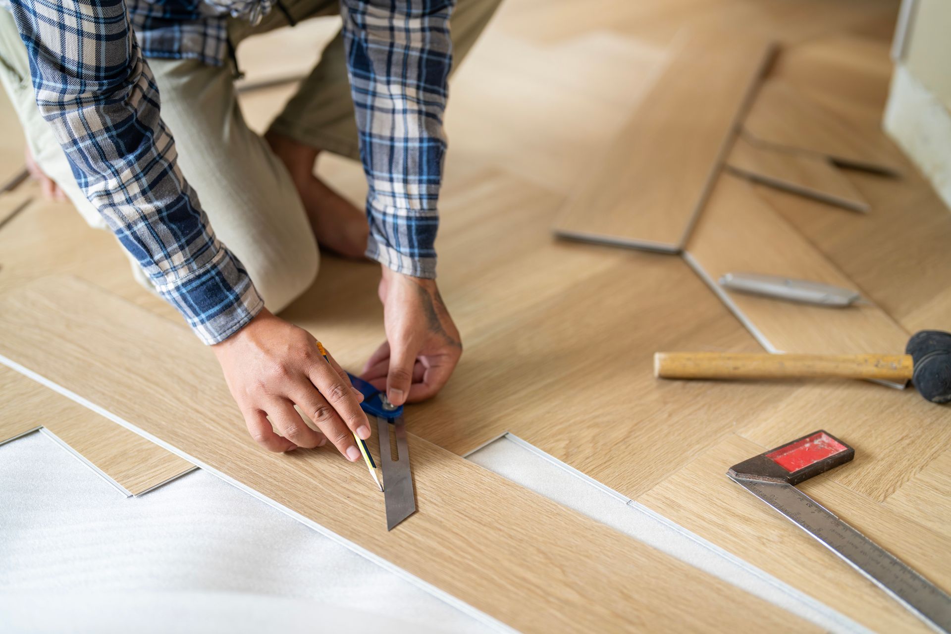 Worker installing laminated luxury vinyl plank flooring indoors.