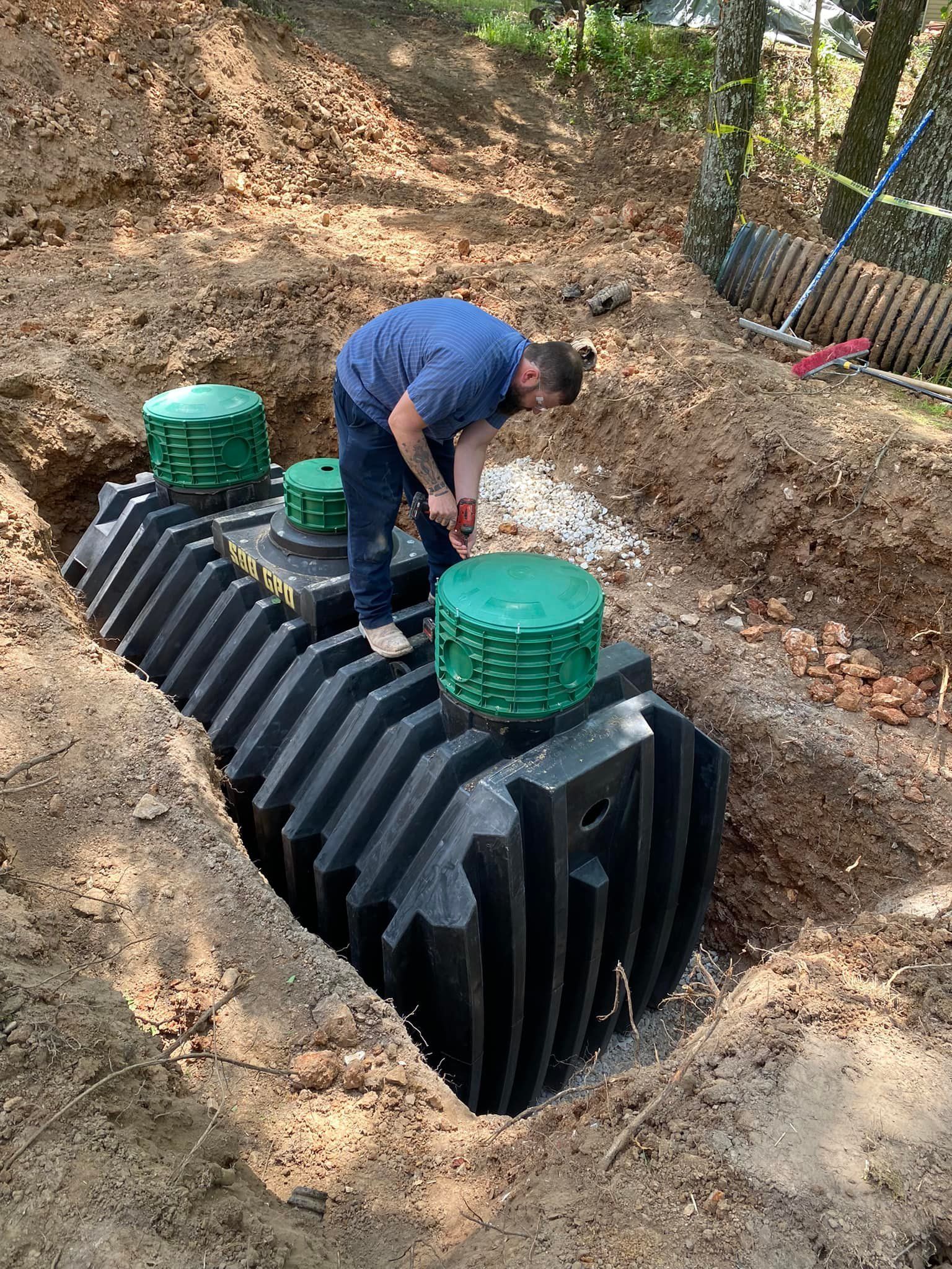 Man working on a black septic tank in a dirt trench, surrounded by green lids.