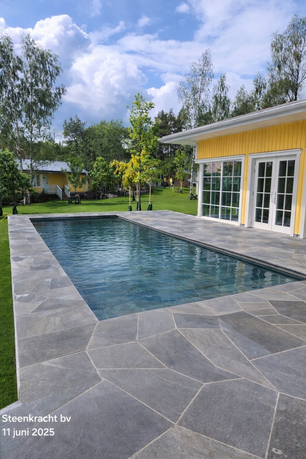 Een rechthoekige MagicPool met een donkerblauwe tegelbodem, naast een geel huis met openslaande deuren.