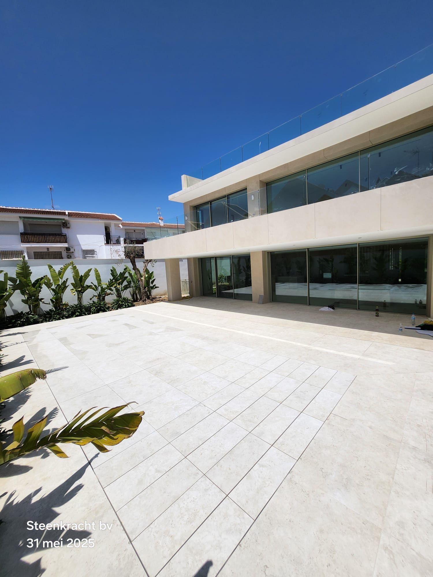 Modern gebouw van twee verdiepingen met grote ramen en een betonnen terras op een heldere zonnige dag. MagicPool