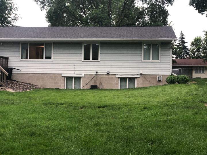 Suburban house with white siding, basement windows, and a large green lawn in front