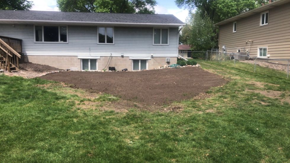 Backyard with a large freshly spread dirt mound behind a gray house and green lawn