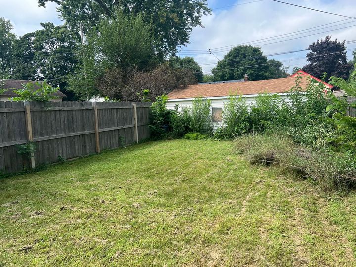 Grassy backyard with wooden fence, trees, and a house in the background