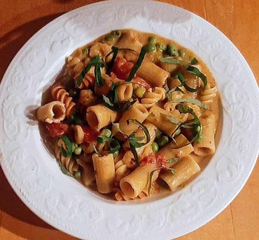 A white plate topped with pasta and vegetables on a wooden table