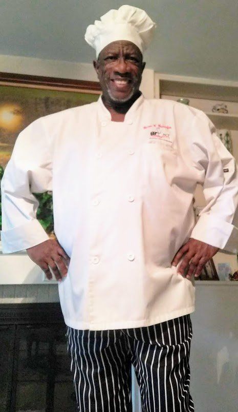 A man in a chef 's uniform is standing with his hands on his hips