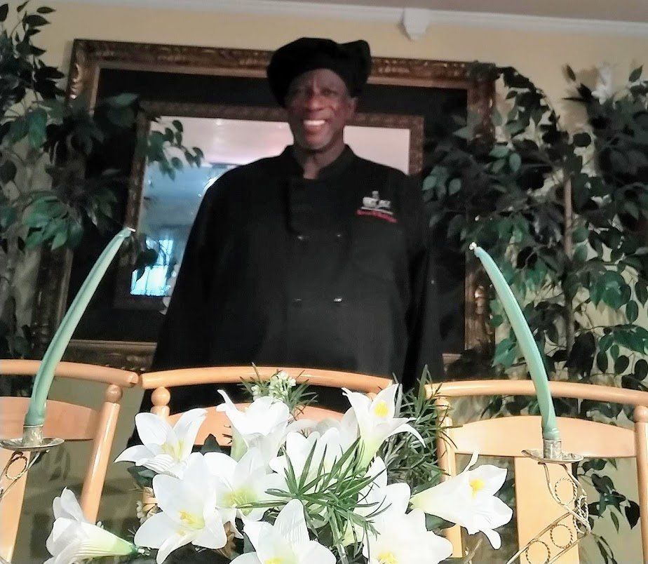 A man in a chef 's uniform stands in front of flowers