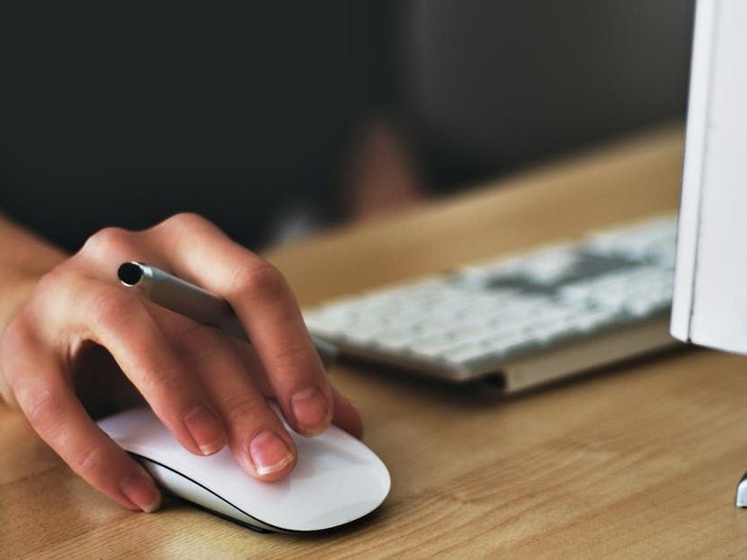 A person is using a computer mouse while holding a pen