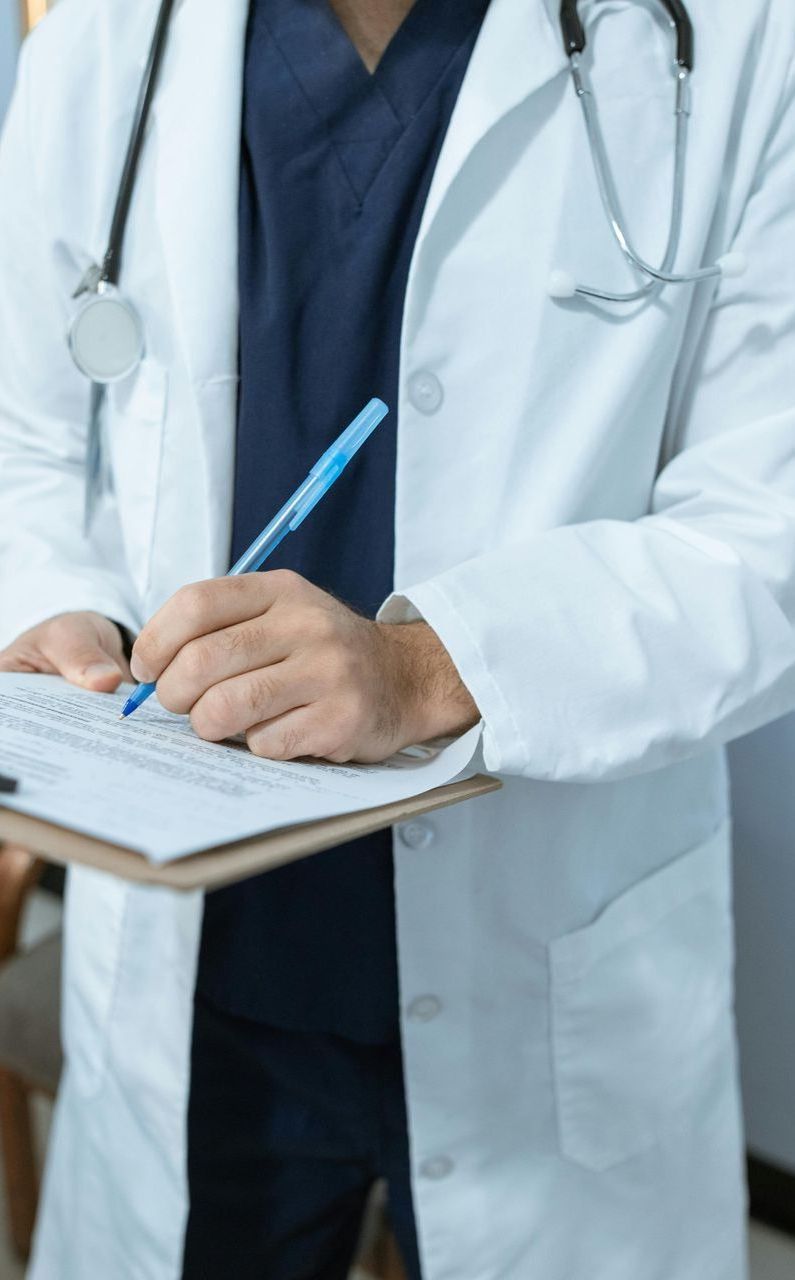 A doctor is writing on a clipboard with a pen.