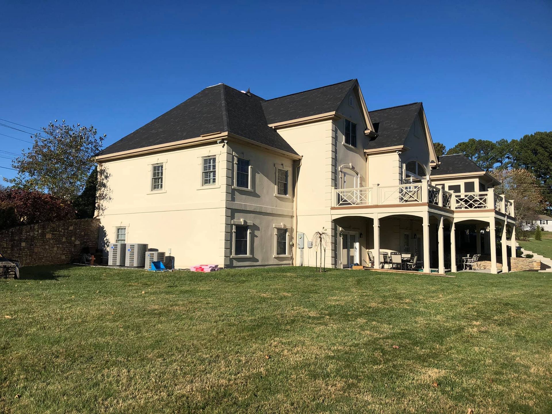 A large white house with a black roof is sitting on top of a lush green field.