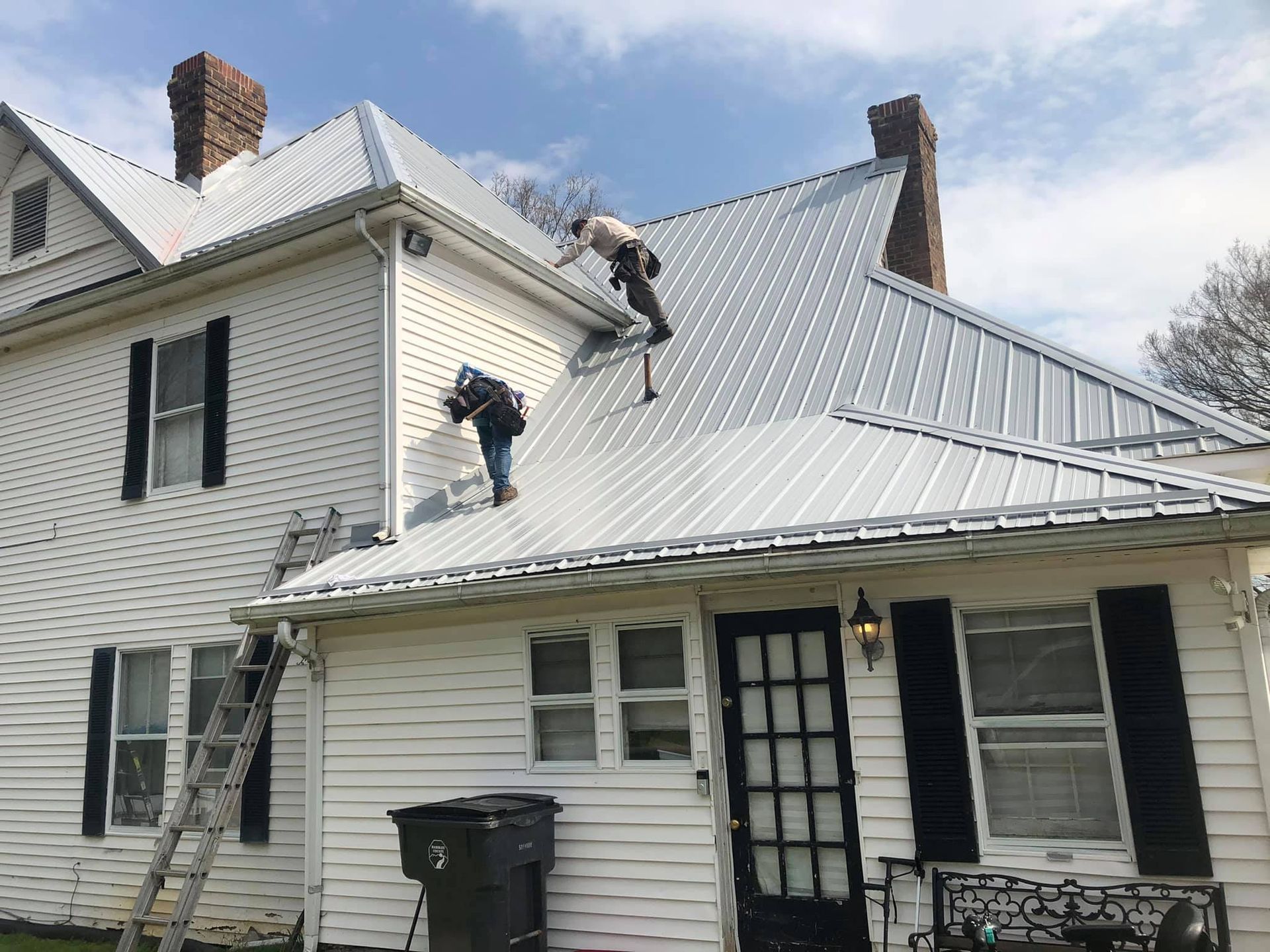 Two men are working on the roof of a white house.
