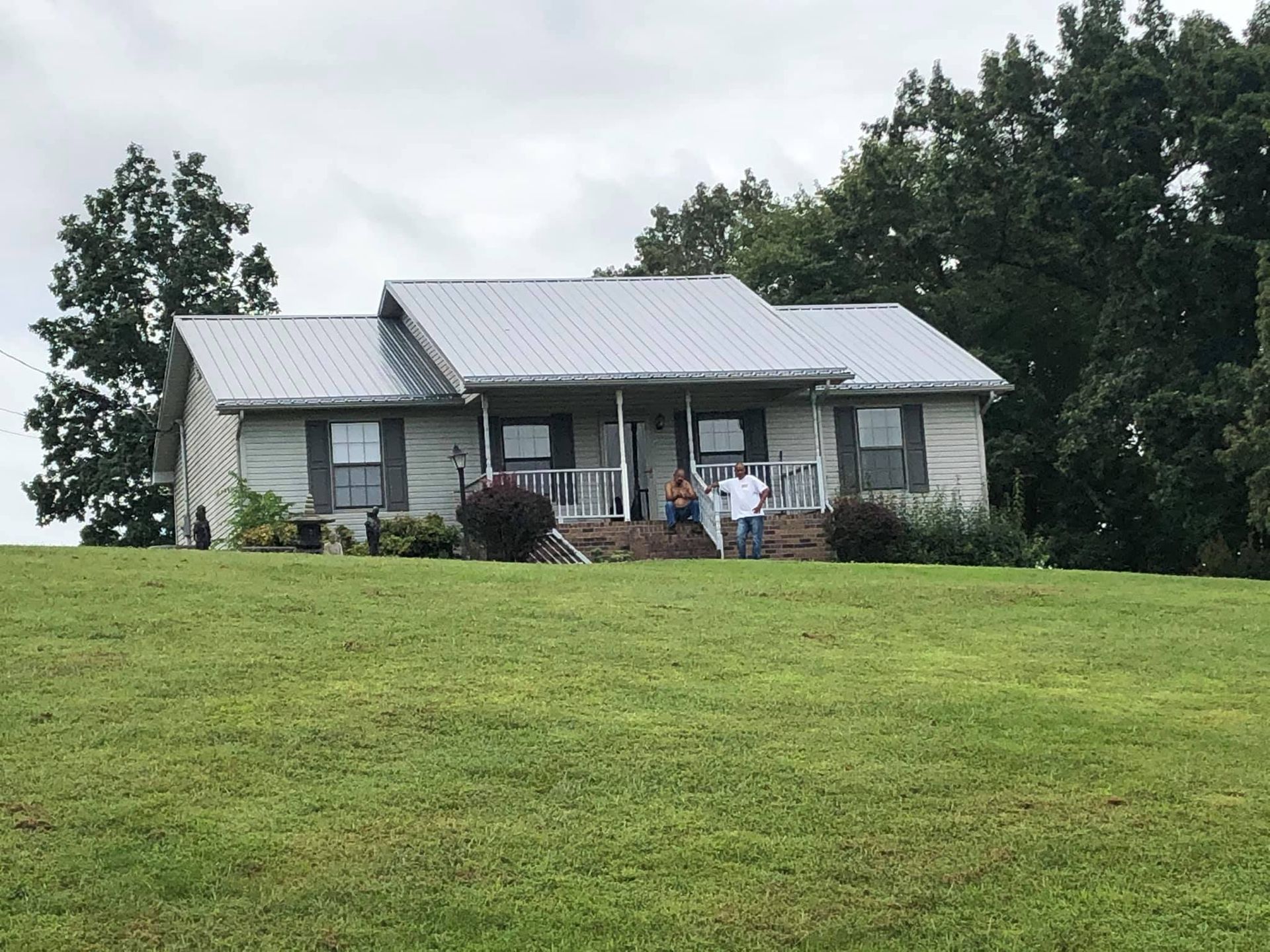 A couple standing in front of a house in a grassy field.