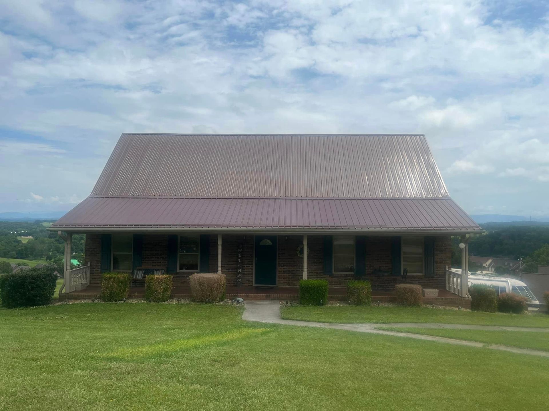 A large house with a metal roof is sitting on top of a lush green hillside.