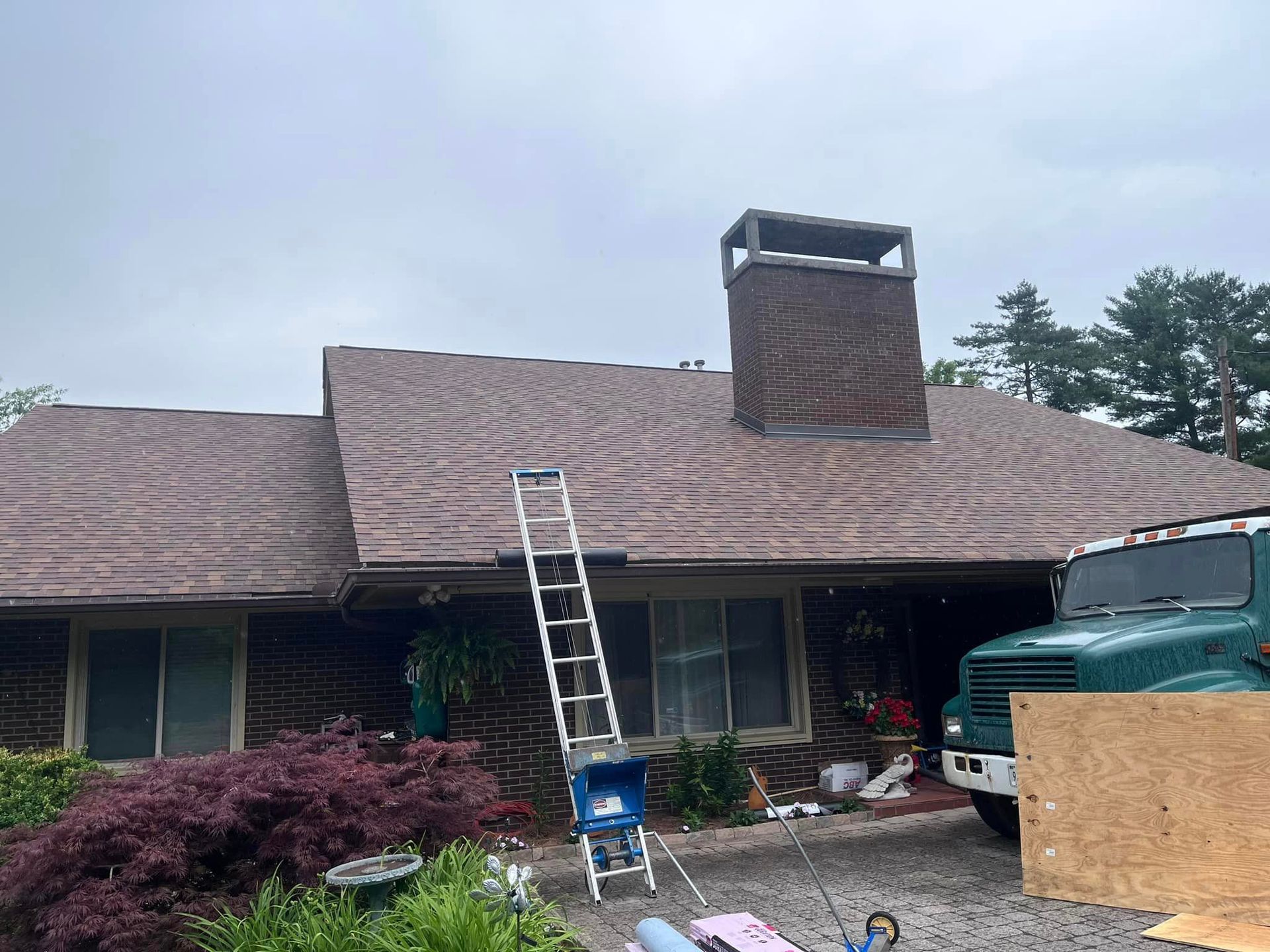 A house with a ladder on the roof and a truck parked in front of it.