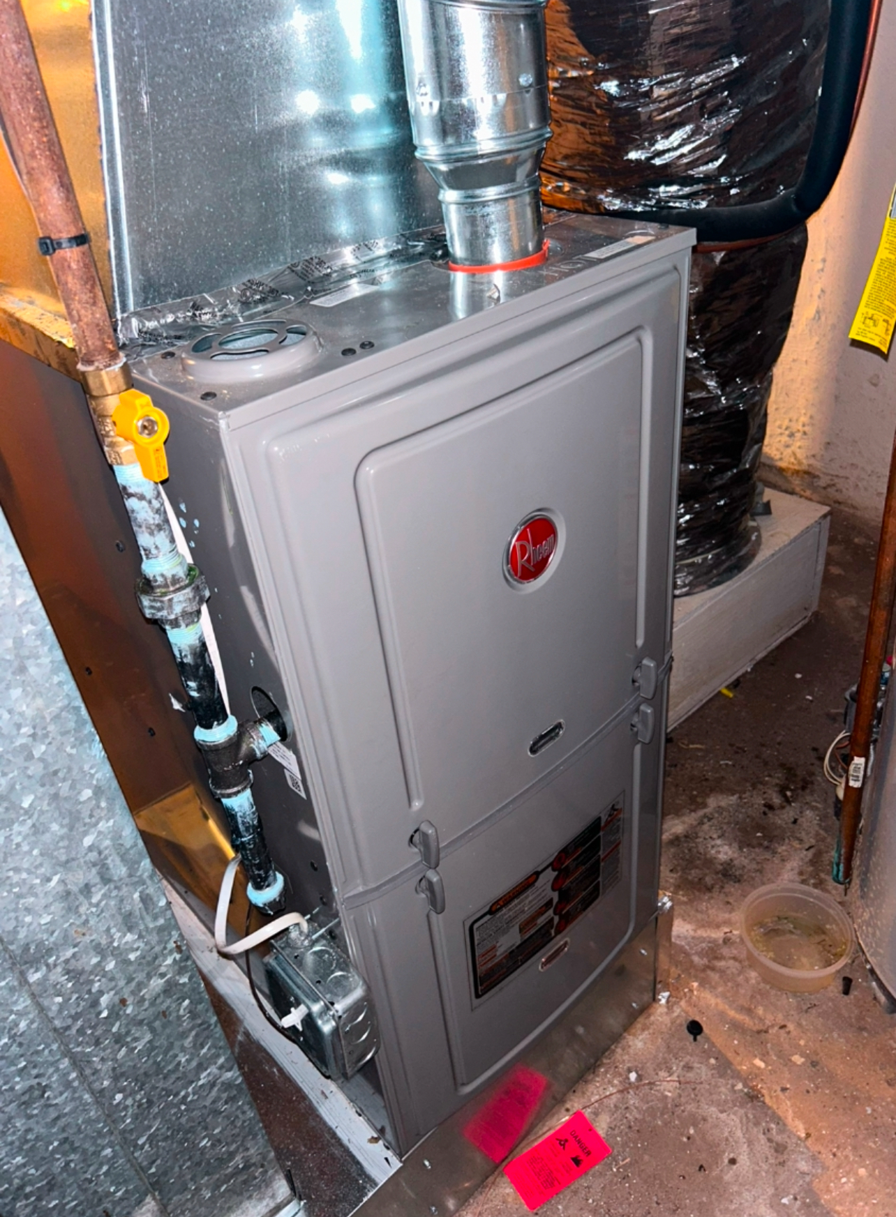 A Rheem gas furnace installed in a utility space, featuring a grey metal cabinet with an attached gas supply line.