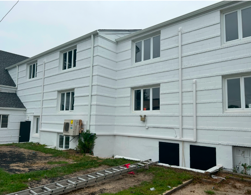 Exterior view of a two-story white house with siding, multiple windows, a foundation level, and an extension ladder.
