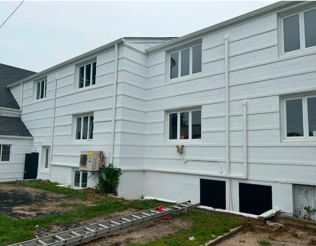 Exterior view of a two-story white house with siding, multiple windows, a foundation level, and an extension ladder.