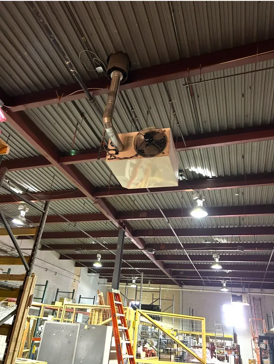 An industrial space showing a heater unit mounted to the corrugated ceiling with a vent pipe extending upward.