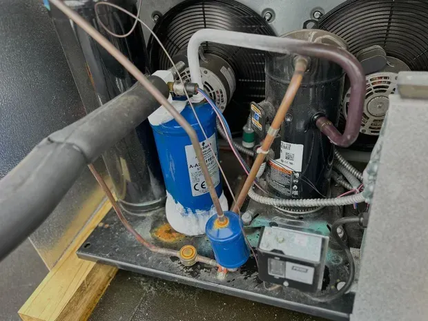 An industrial refrigeration unit with blue filters, copper tubing, and fans, showing heavy frost buildup on the components.