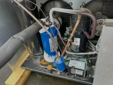 An industrial refrigeration unit with blue filters, copper tubing, and fans, showing heavy frost buildup on the components.