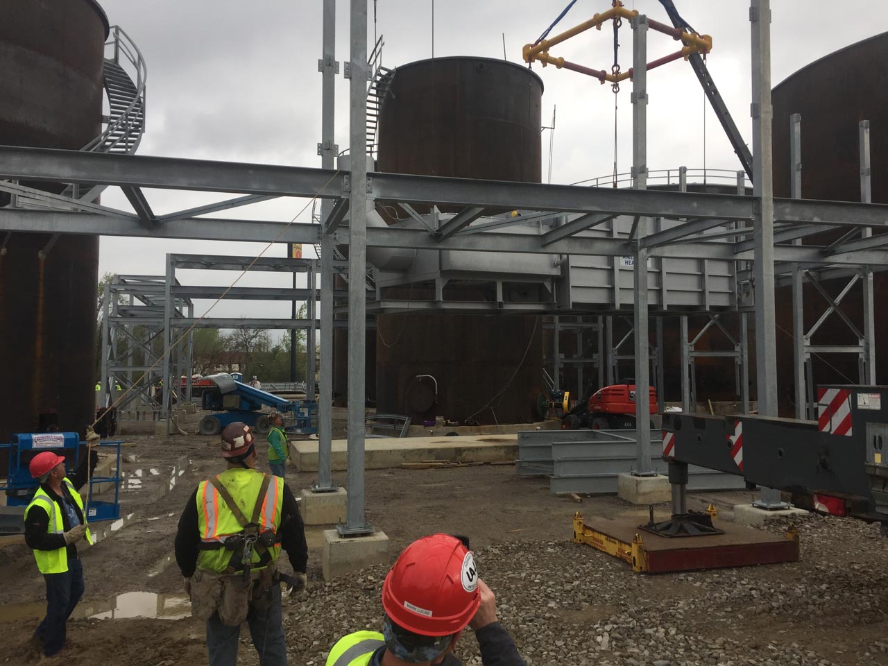 Construction site with workers, steel framework, storage tanks, and a crane.