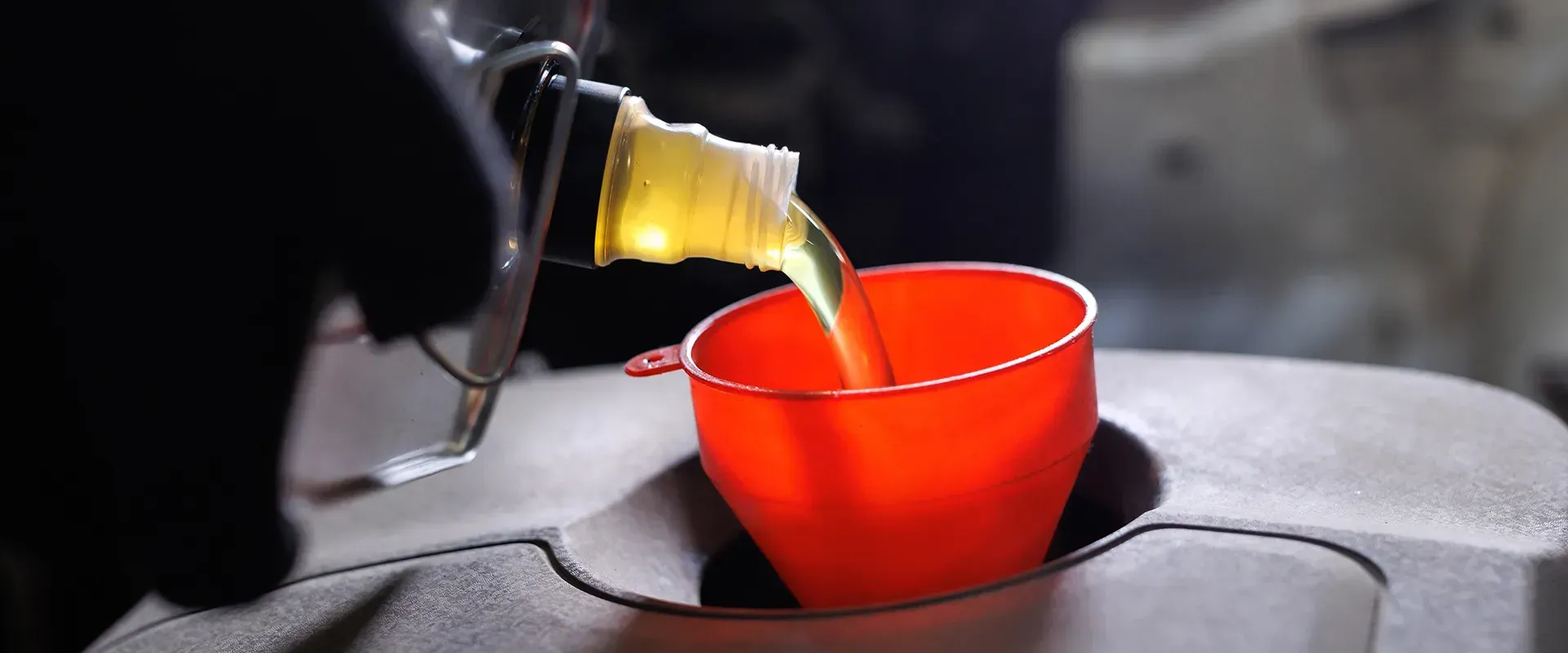 Oil being poured from a bottle into an orange funnel in an engine bay.