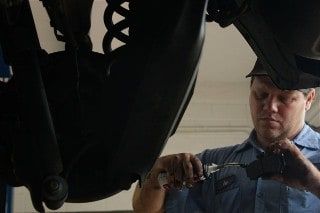 Mechanic working on the underside of a car, using a tool.