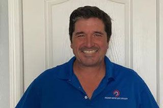 Man in blue polo shirt smiles in front of a white door.