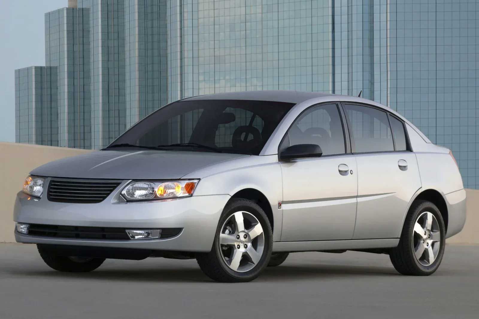 Silver Saturn Ion sedan parked in front of a modern building with many windows.