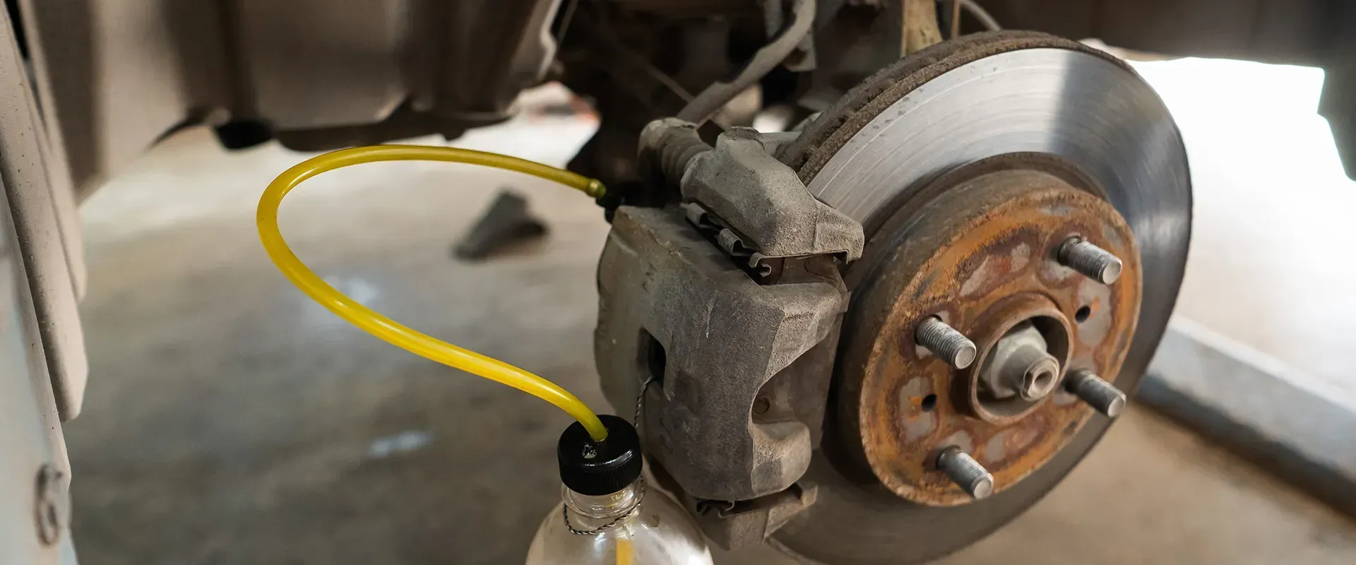 A car's brake disc with a yellow hose connected, bleeding brake fluid into a bottle.