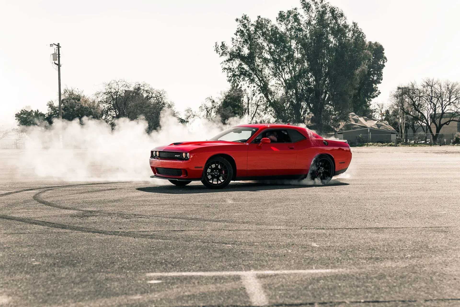 Red Dodge Challenger performing a burnout, creating smoke on asphalt.